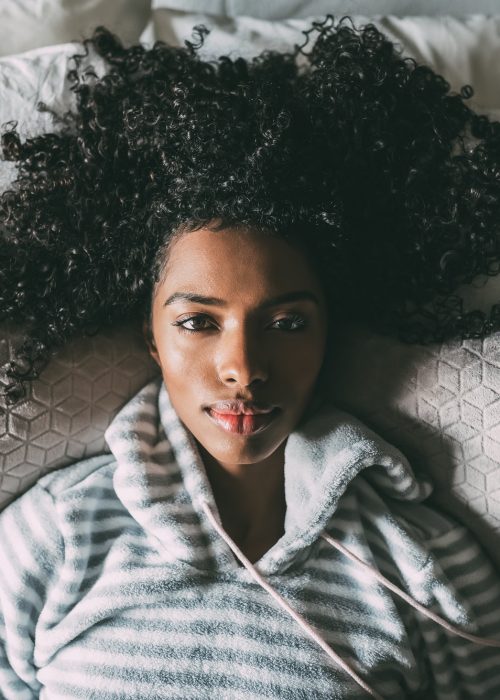 Beautiful black woman with curly hair lying on bed looking at the camera